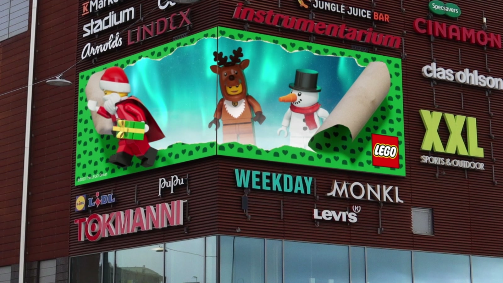 LEGO holiday characters bursting out of a green wrapped billboard